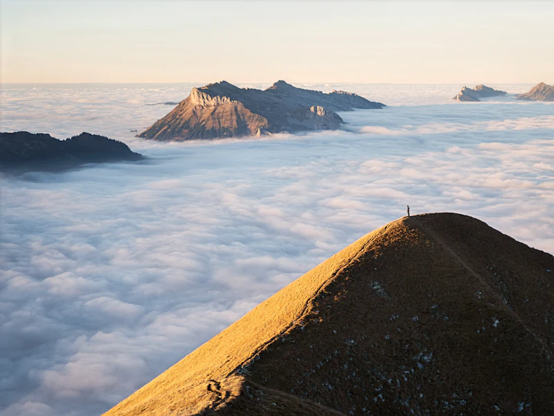 Einzelne Person auf einem Gipfelgrat über einem Wolkenmeer
