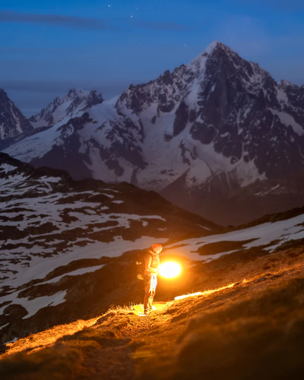 Person mit Stirnlampe auf einem Bergpfad in der Dämmerung